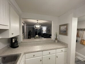 A kitchen with white cabinets, a coffee maker, and a dining area with a sofa and a chandelier.