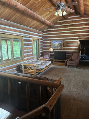 Cozy cabin interior with exposed beams, comfortable seating area, and a flat-screen TV.