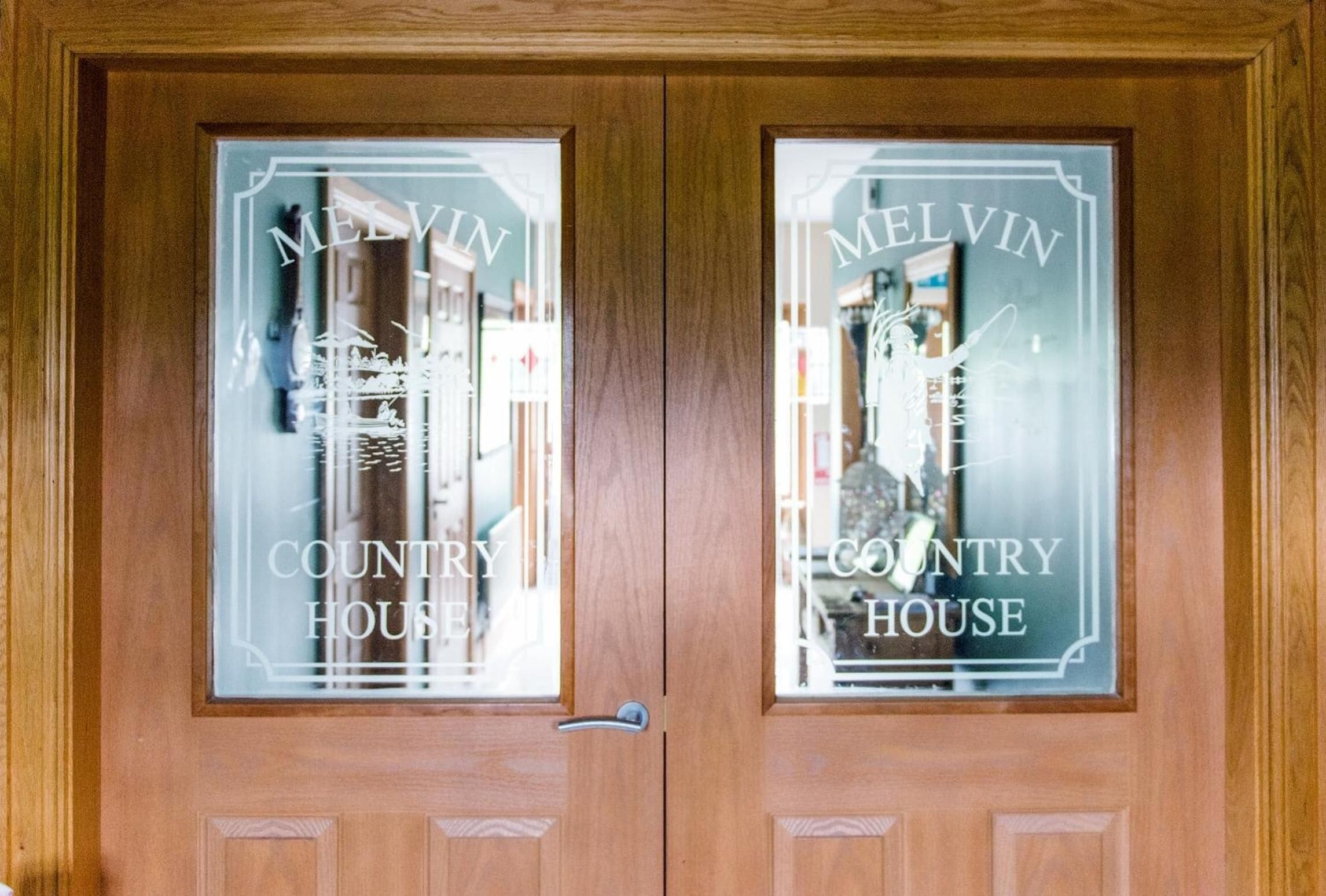 Una puerta doble de madera con paneles de vidrio esmerilado que muestra el texto "MELVIN COUNTRY HOUSE".
