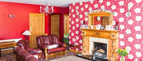 Una habitación con pared roja, chimenea, sofá de cuero y papel tapiz estampado.