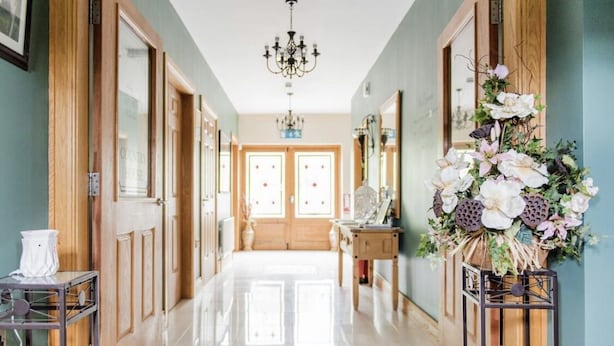 A hallway with wooden doors, a chandelier, and a floral arrangement.