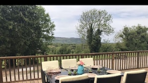 A deck with outdoor furniture, including a table and chairs, set against a backdrop of trees and a distant view.