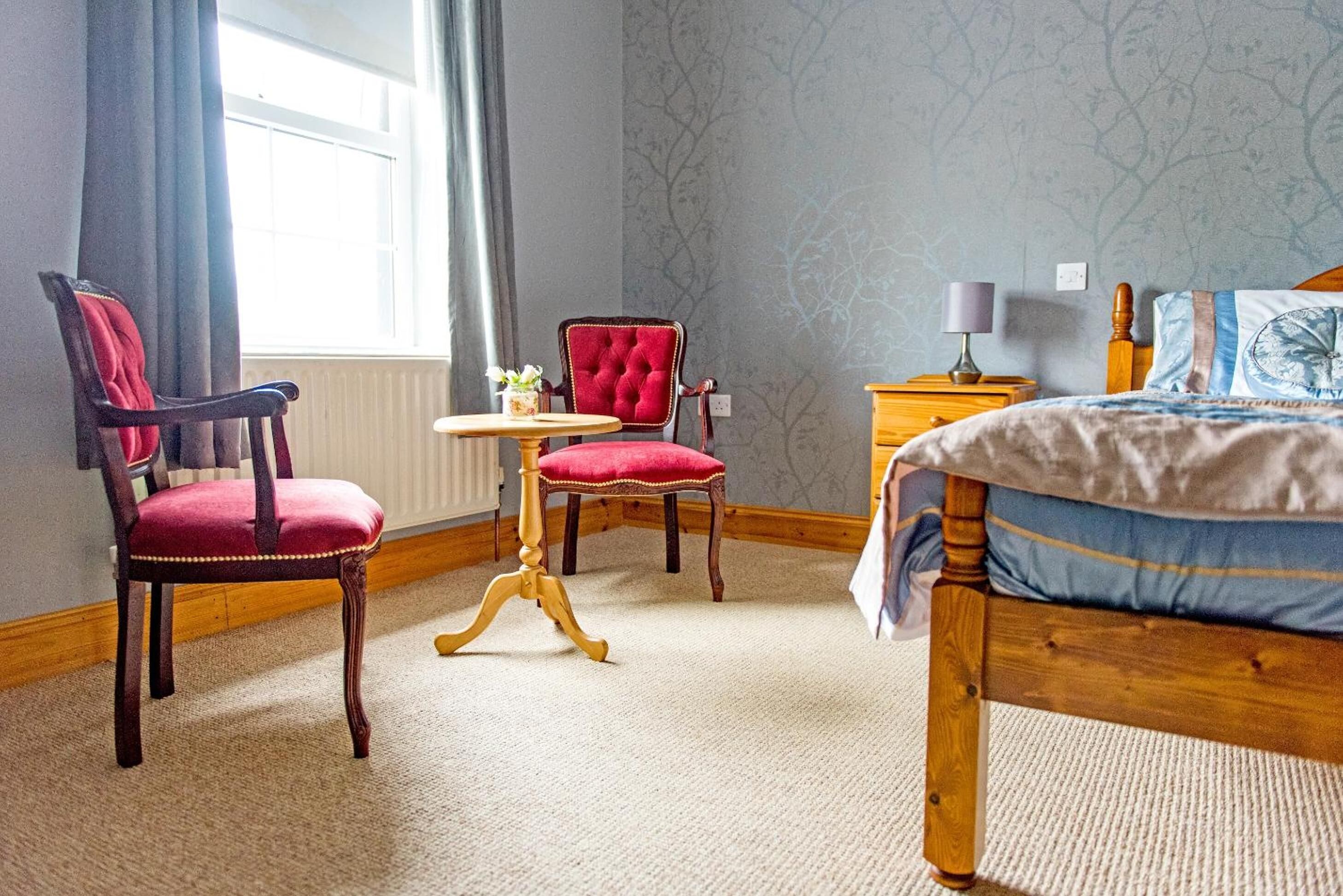 A bedroom with a bed, two chairs, a small table, and a nightstand.