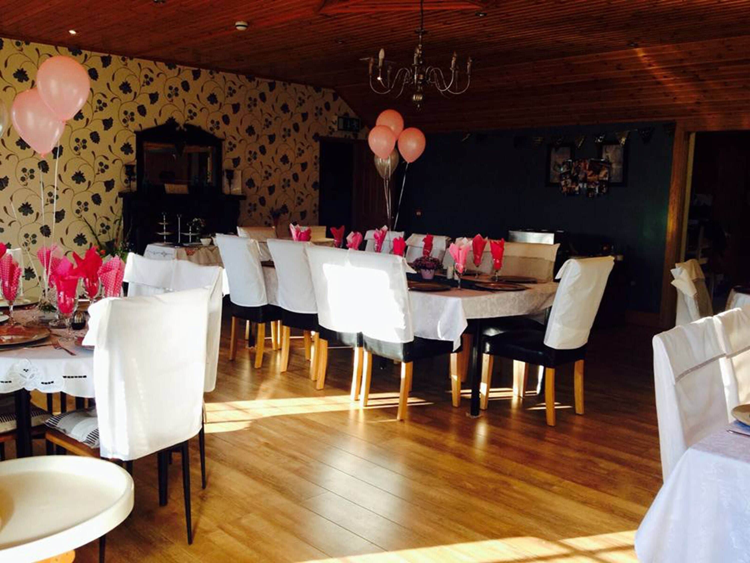 A dining area with white tables and chairs, a wooden floor, and a chandelier.