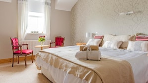 A hotel room with a large bed, two chairs, a small table with flowers, and a window with curtains.