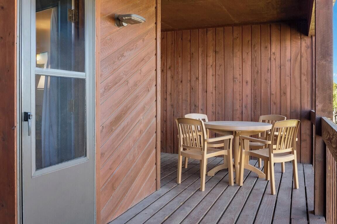 A wooden deck with a table and chairs, a door with a glass panel, and a wooden wall.