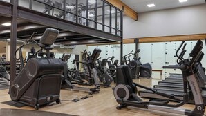 Un gimnasio con diversas máquinas de ejercicio, piso de madera y un entresuelo.
