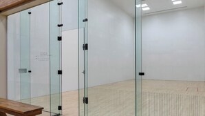 Una habitación con paredes de vidrio, un banco de madera y suelo blanco.