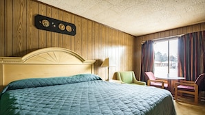 A hotel room with a large bed, wooden panel walls, a small table with chairs, and a window with curtains. - OYO Hotel Holly Springs MS (Holly Springs)