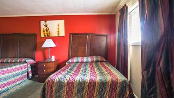 A room with two beds, a dresser, a lamp, and a painting on the wall.