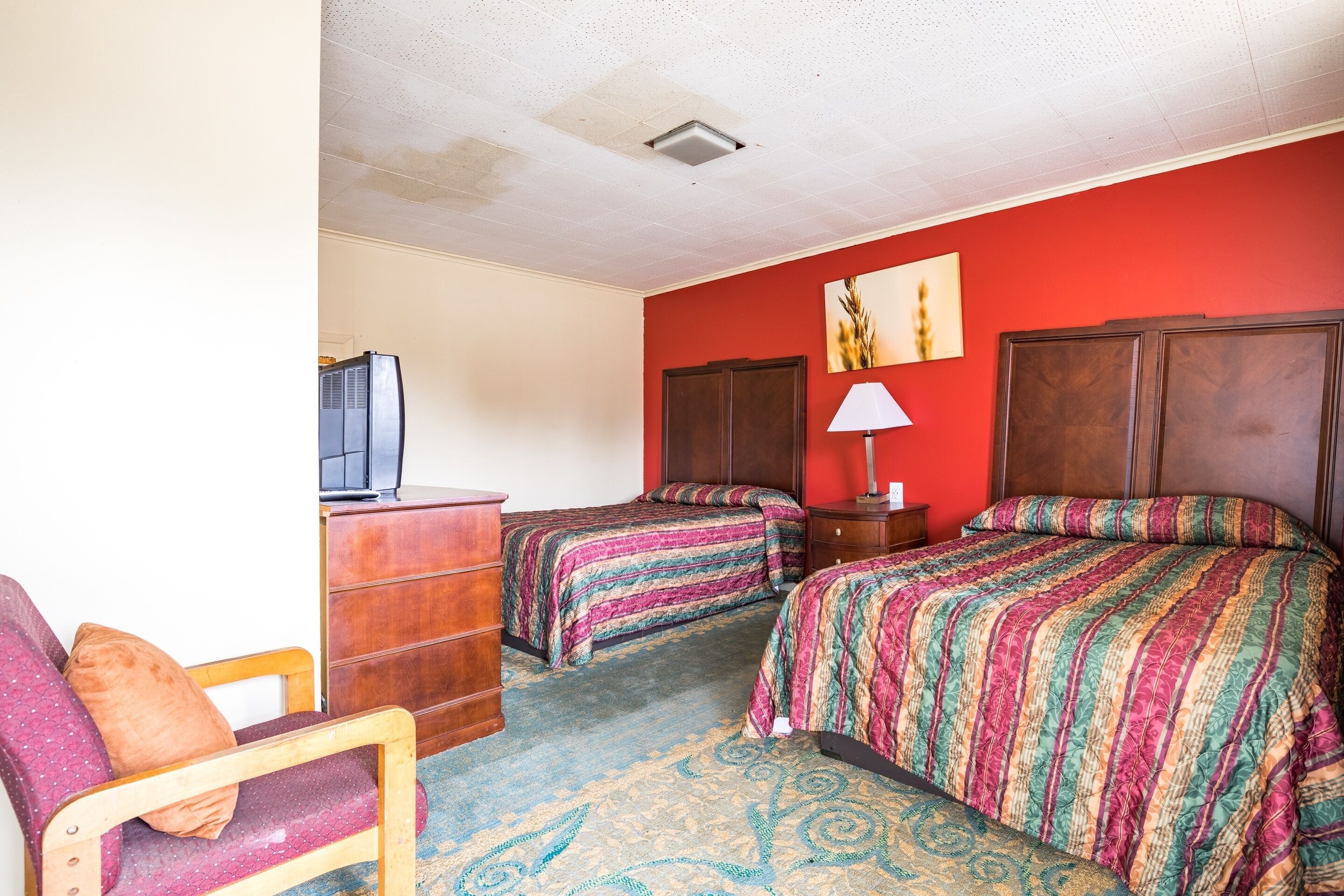 Una habitación de hotel con dos camas, una silla de madera, un aparador y un televisor.