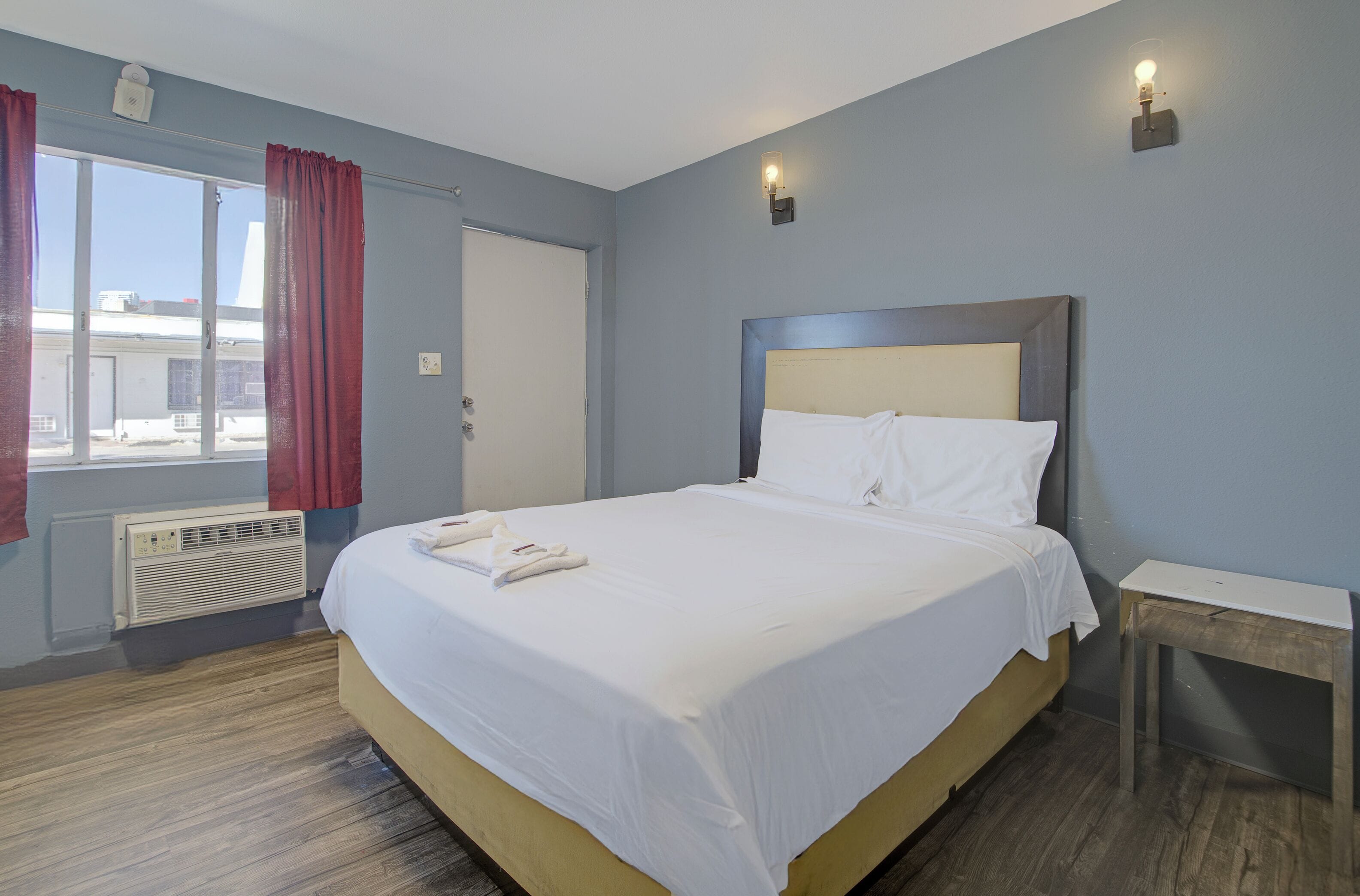 Habitación de hotel con una cama grande, una mesita de noche, una ventana con cortinas y un aplique de pared.