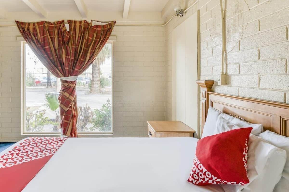 Habitación de hotel con cama, ventana con cortinas, mesita de noche de madera y pared de ladrillo.