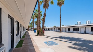 Une rangée de chambres d’un motel à un seul étage, avec un parking devant, des palmiers et un ciel bleu dégagé.