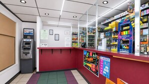 Un kiosque situé à l’intérieur, avec un comptoir rouge, un distributeur automatique de billets et différents présentoirs de produits.