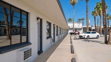 A building with a row of windows and a parking area with a white car and a red vehicle.