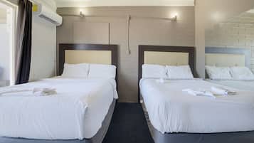 Habitación de hotel con dos camas, cada una con ropa blanca y almohadas, una pared de ladrillo y un equipo de aire acondicionado.