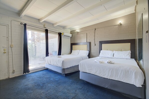 A hotel room with two beds, a window with curtains, an air conditioning unit, and a blue carpet. - OYO Oasis Motel Las Vegas I-15 (Las Vegas)