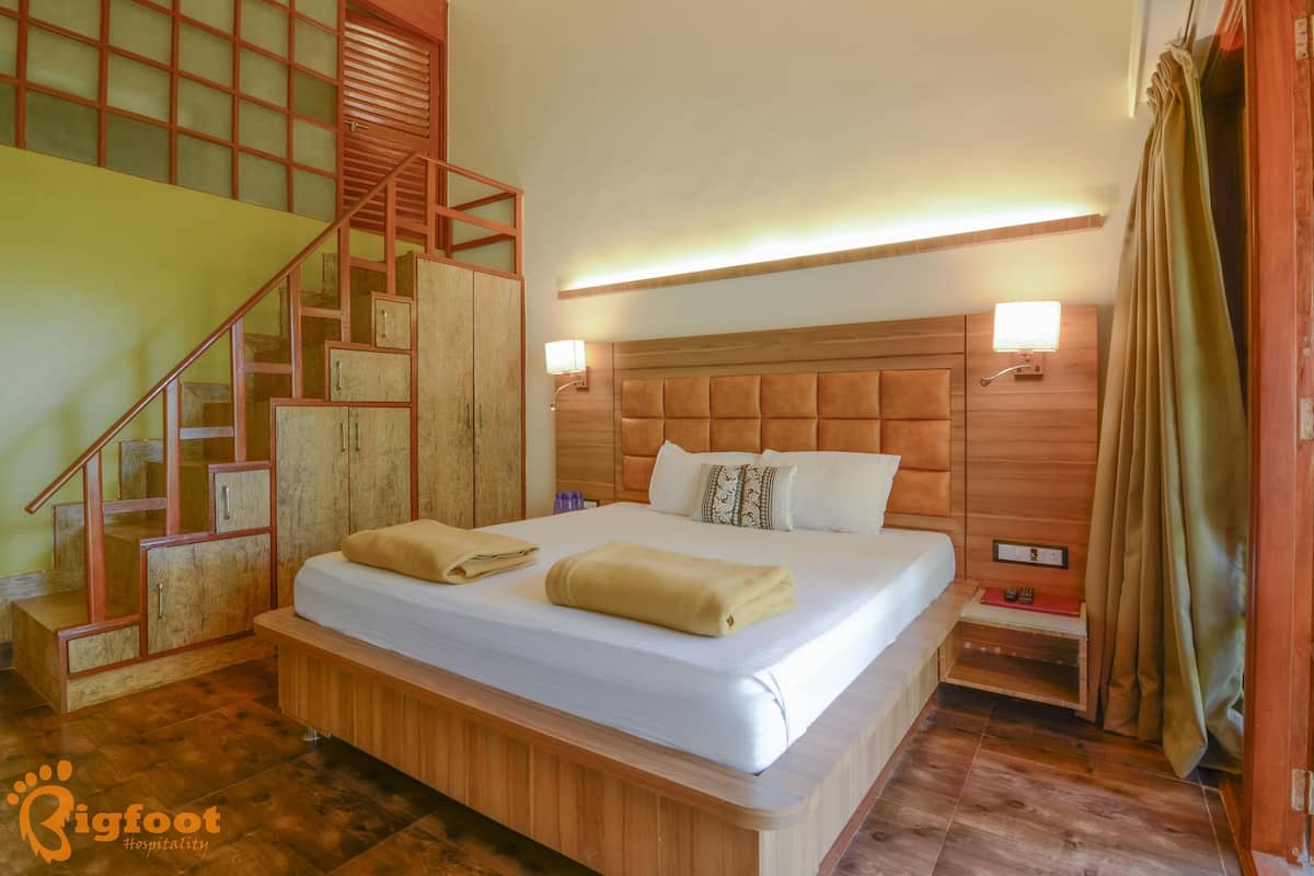 Une chambre d’hôtel avec un grand lit, une tête de lit en bois, deux lampes de chevet, une table de chevet et un escalier avec une rampe en bois.