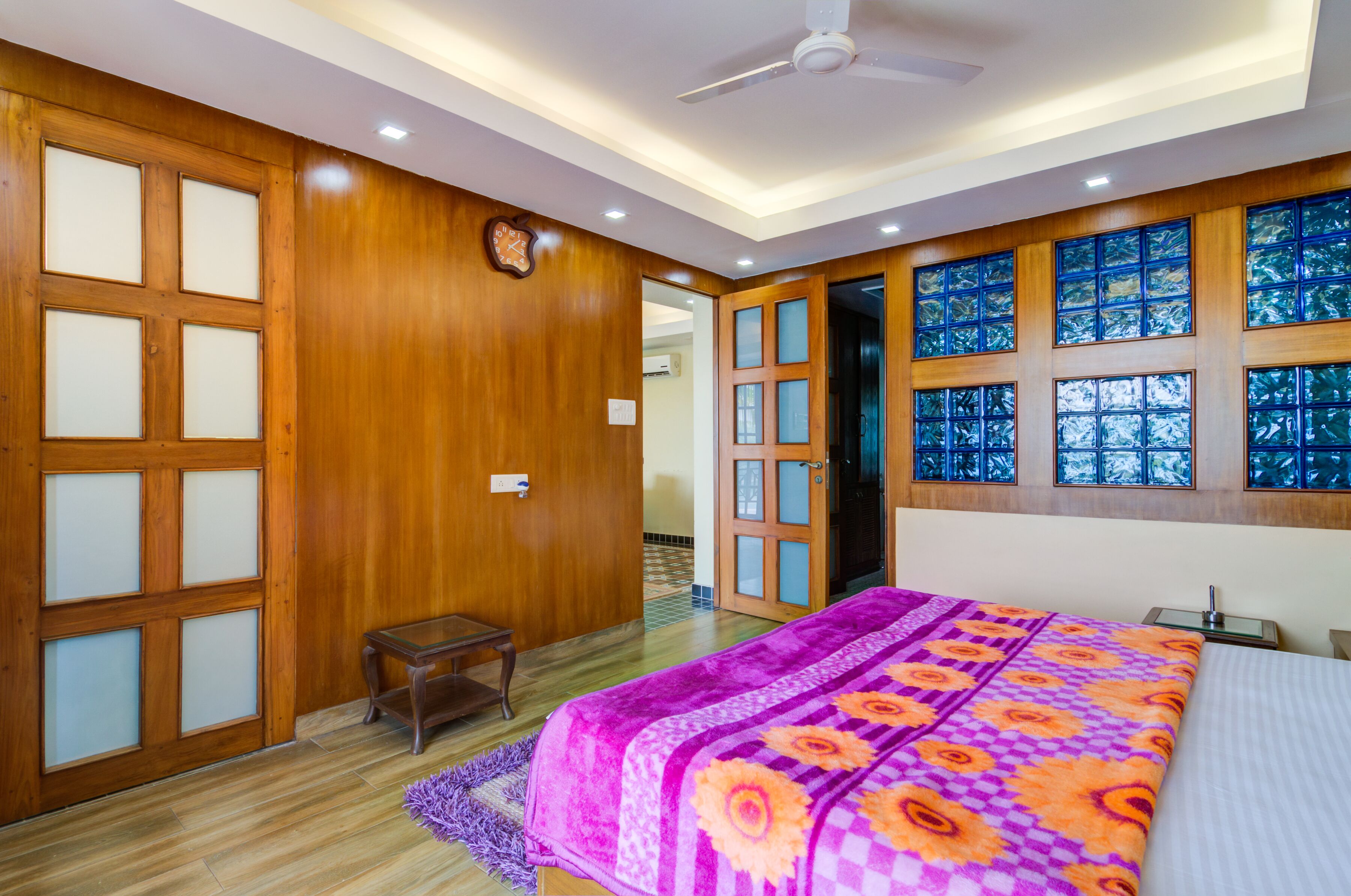 A bedroom with a large bed, wooden paneling, a small table, and a ceiling fan.