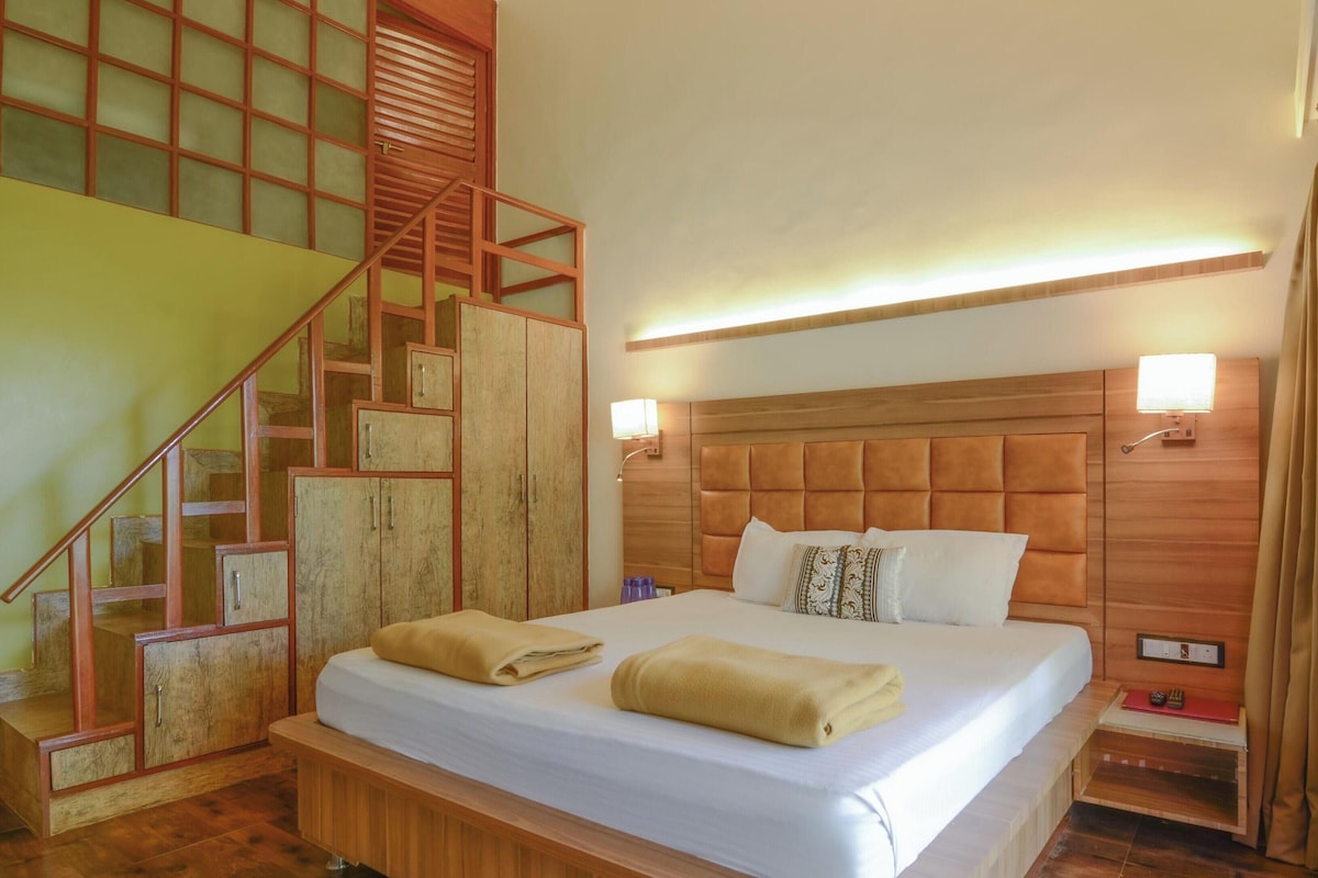 A bedroom with a bed, a wooden headboard, a staircase, and a nightstand with a lamp.