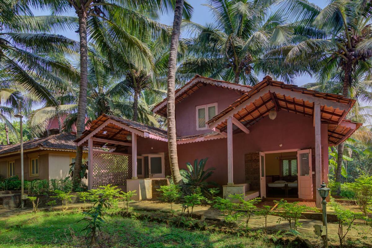 Une maison de style bungalow avec un toit en tuiles, une véranda et un jardin agrémenté de palmiers et de plantes.