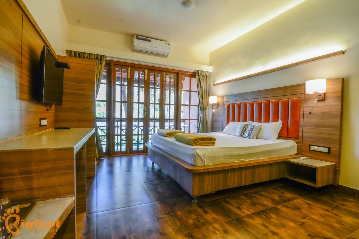Une chambre d’hôtel avec un lit en bois, un bureau, une télévision et une fenêtre avec des rideaux.