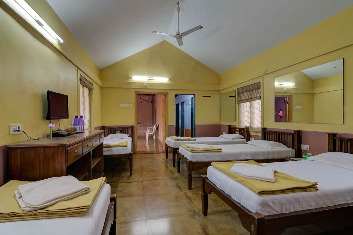Une chambre d’hôtel avec quatre lits, un bureau avec un ordinateur, un miroir et un ventilateur de plafond.