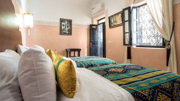 Habitación de hotel con dos camas, zona de estar y ventana con cortinas.