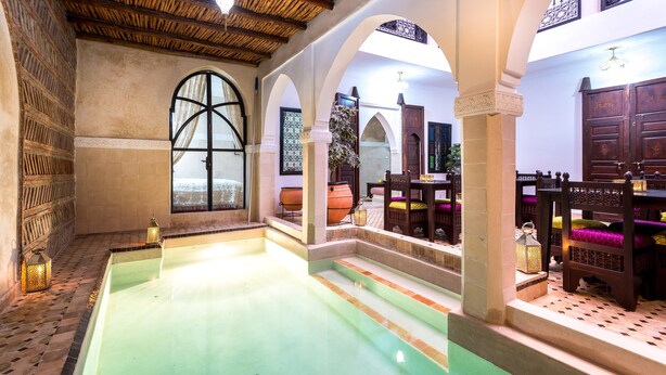 Un interior marroquí tradicional amb piscina, arcs de fusta i parets revestides de rajoles.