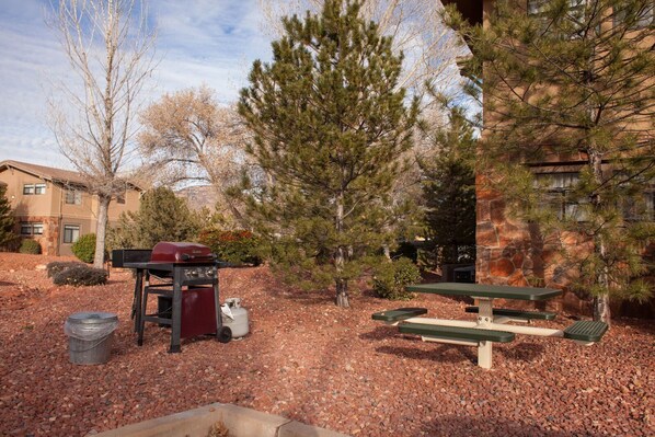 Un patio al aire libre con una parrilla, mesas de picnic y un muro de piedra.
