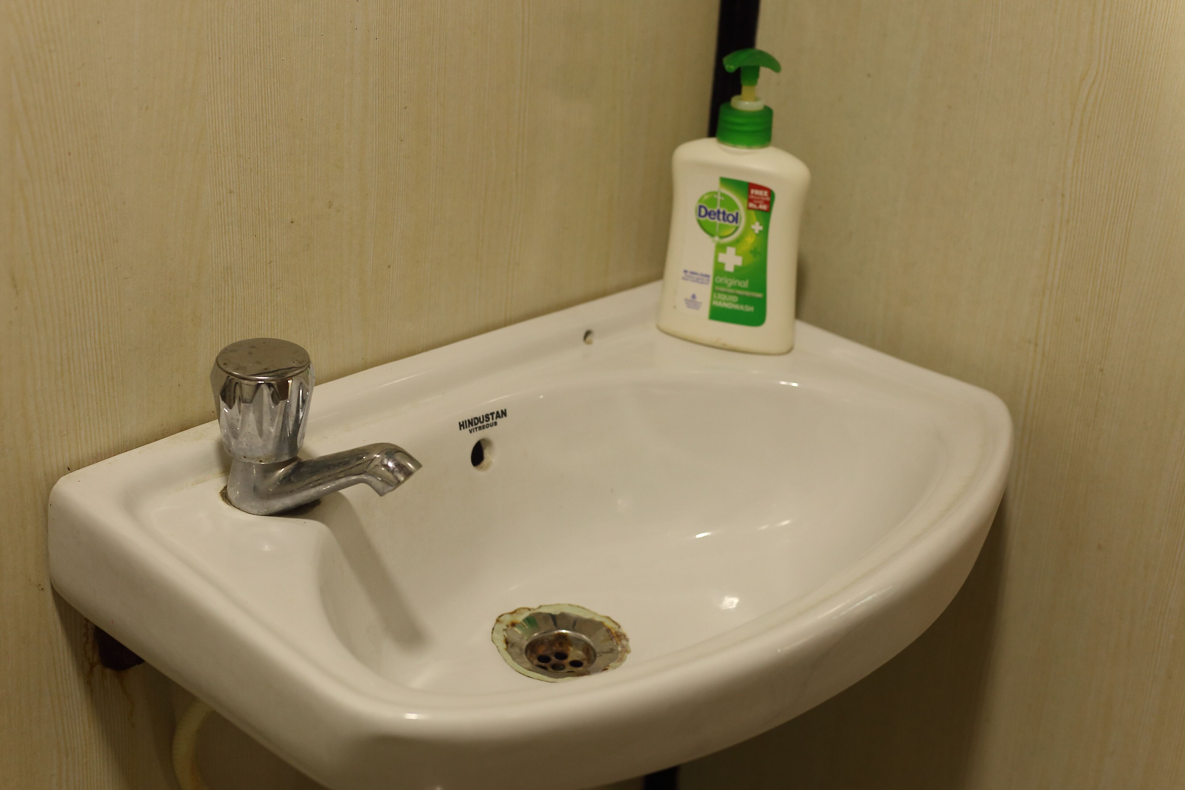 A white bathroom sink with a single faucet and a bottle of Dettol soap.
