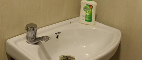 A white bathroom sink with a single faucet and a bottle of Dettol soap.