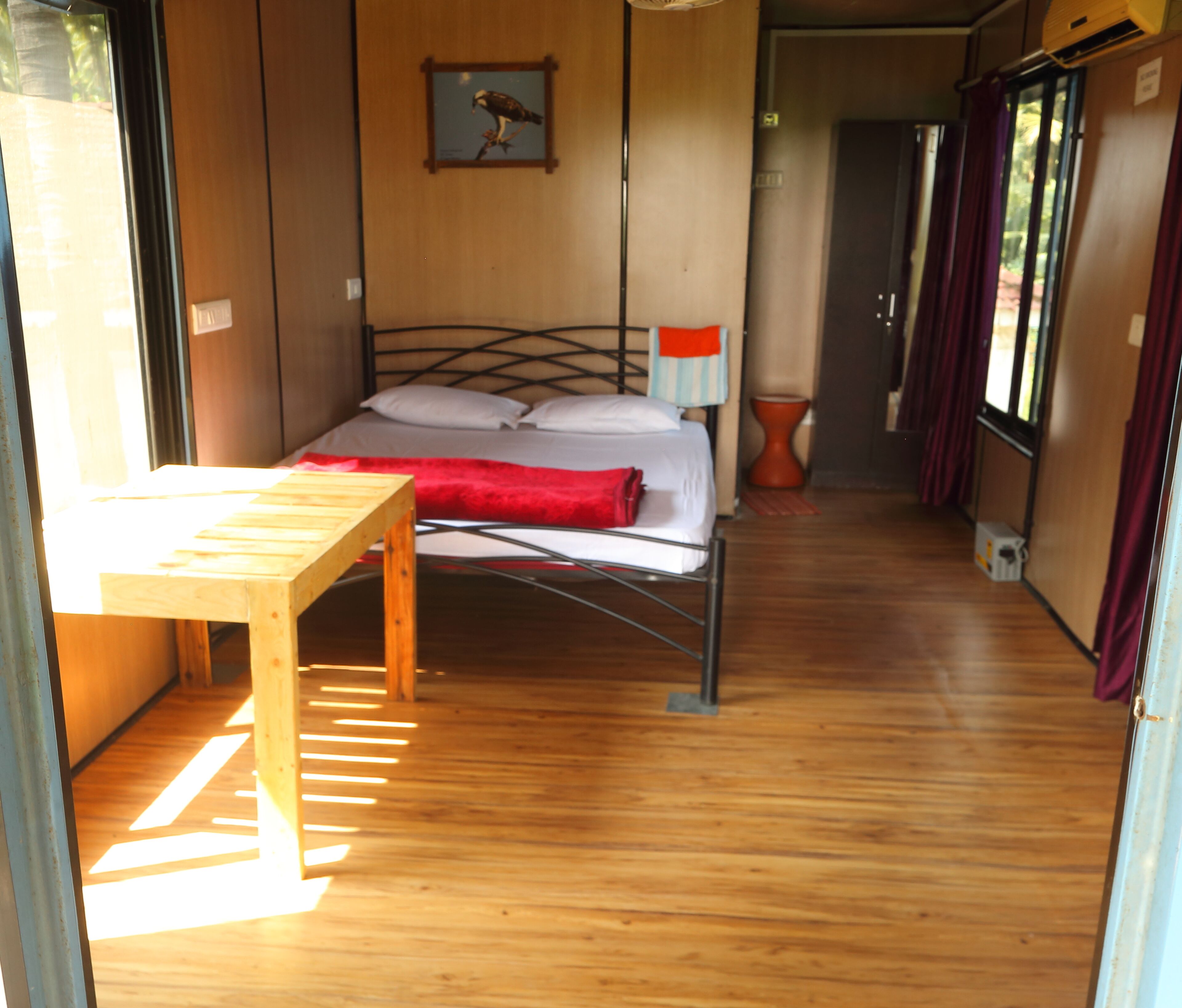 A room with a bed, a wooden table, and a painting on the wall.