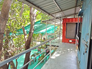 A covered outdoor area with a metal roof, a green tarp, and a red wall. - IORA Cottages (Alibag)