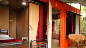 A room with a bed, a chair, and a table. There are doors leading to other rooms. - IORA Cottages (Alibag)