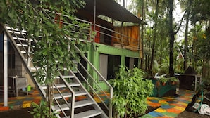 A staircase leading to a green-roofed building surrounded by lush greenery. - IORA Cottages (Alibag)