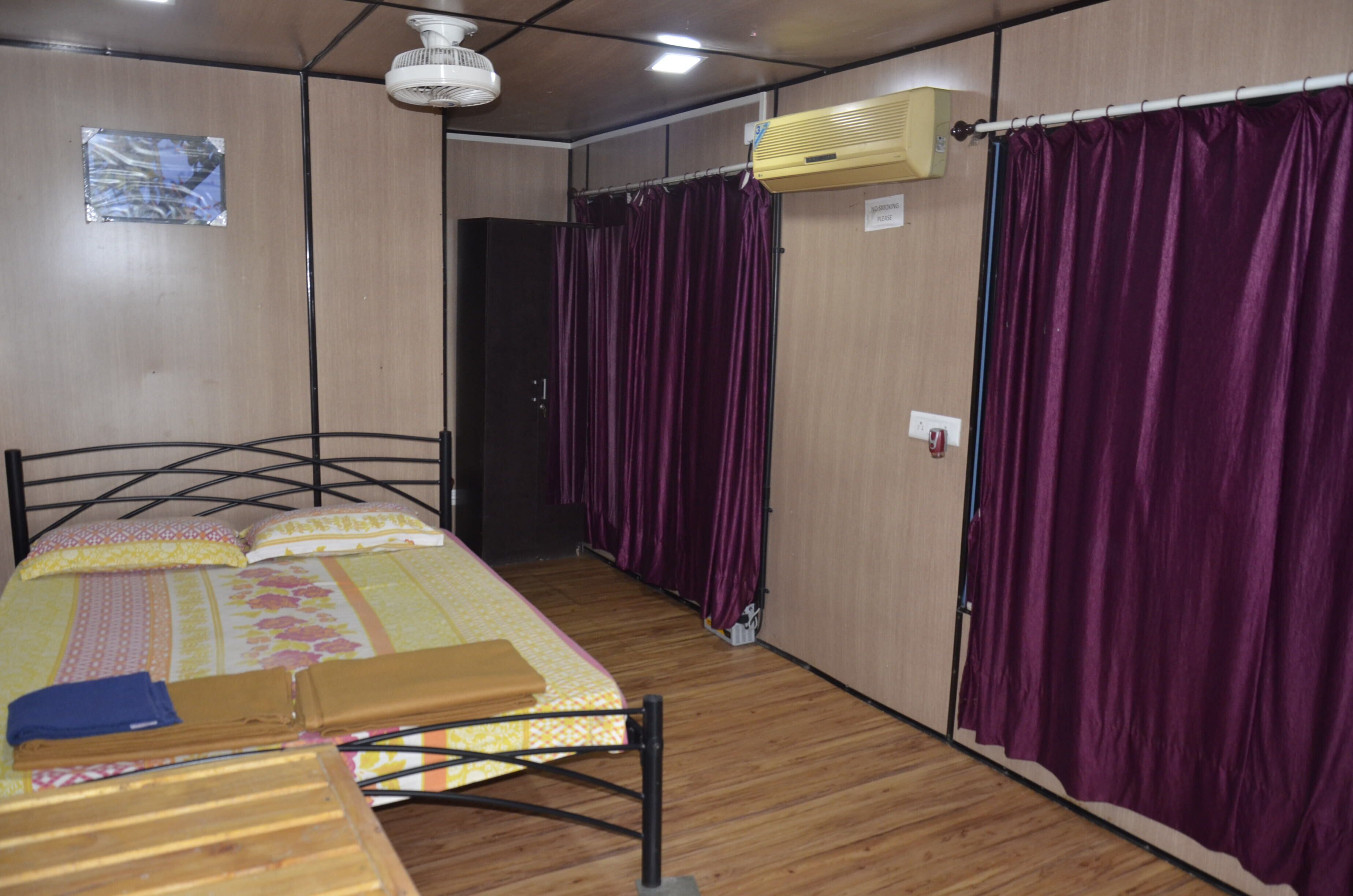 A room with a bed, a wooden floor, a ceiling fan, an air conditioning unit, and purple curtains.