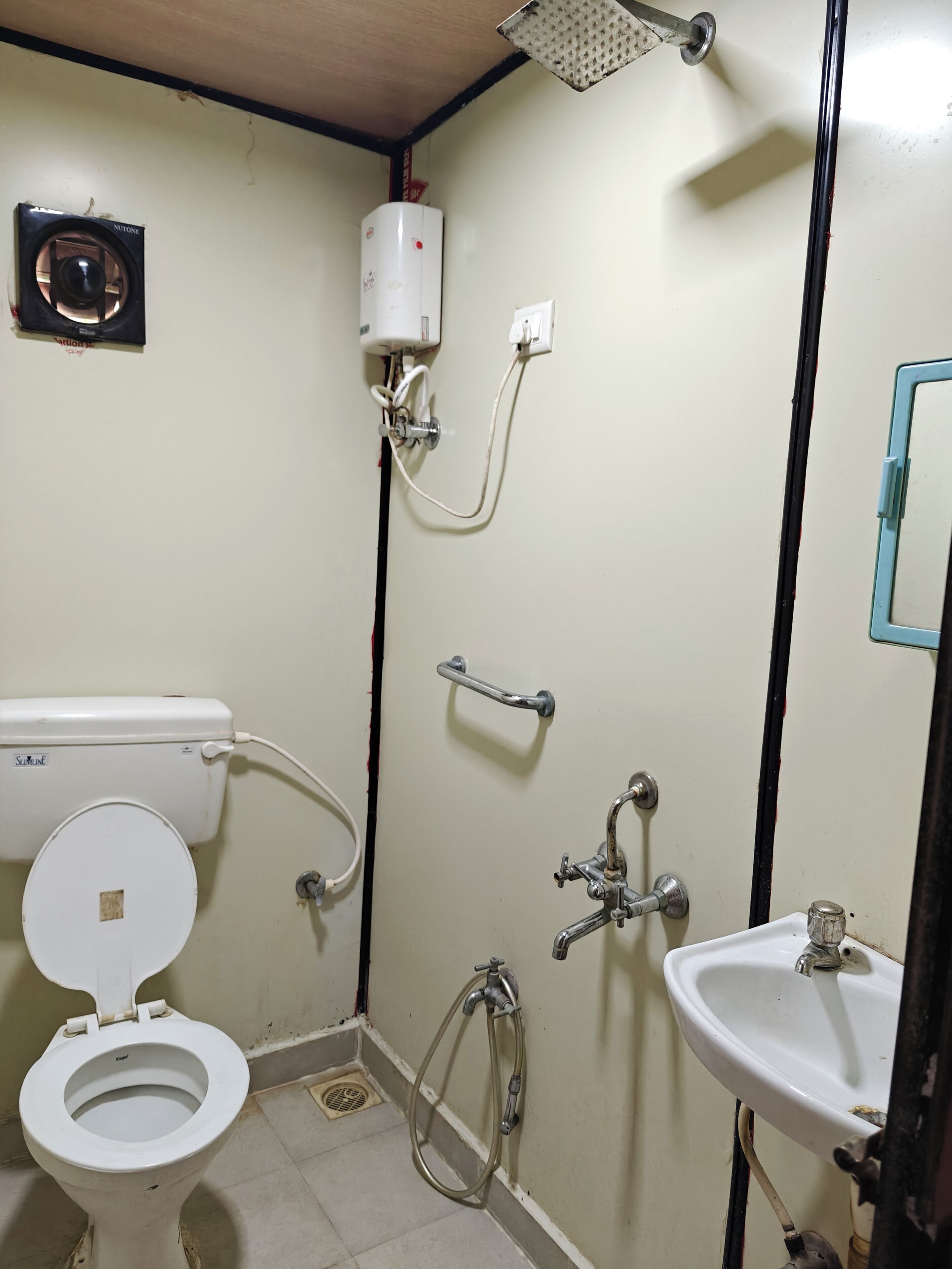Un baño pequeño y sencillo con inodoro, lavamanos, ducha y un calentador.