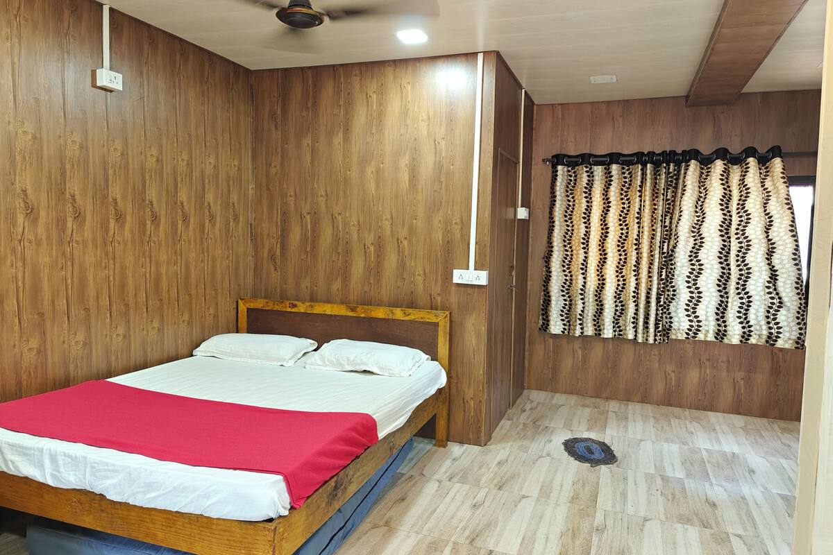 A bedroom with a wooden headboard, a bed with white and red bedding, a ceiling fan, and a patterned curtain.