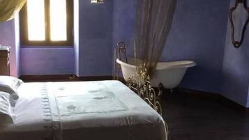 A bedroom with a bed, a window with curtains, a bathtub, and a hanging light fixture.