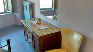 A room with a marble vanity, a yellow chair, a wooden cabinet, and a large mirror on the wall. - Antica Taverna del Principe (Sepino)
