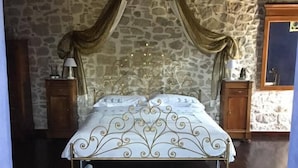 A bedroom with a stone wall, a bed with a decorative headboard, two bedside tables with lamps, and a chair. - Antica Taverna del Principe (Sepino)