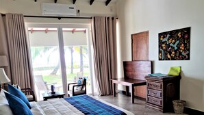 A hotel room with a bed, a desk, and a chair. There is a window with curtains, a painting on the wall, and a view of the outdoors. - Arhimser Villa (Kahandamodara)