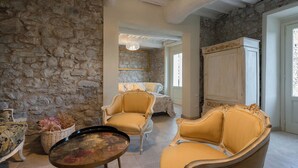 A room with stone walls, a large cabinet, two ornate chairs, a table with flowers, and a hanging light fixture. - Casa Collodi Castello (Collodi)
