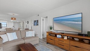 Una sala de estar con un televisor de pantalla plana grande, un mueble de entretenimiento de madera, un sofá color beige y una mesa de centro.