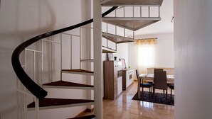 Un escalier en colimaçon mène à un espace cuisine comprenant une table et des chaises.