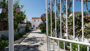 Un chemin pavé, bordé de rambardes métalliques blanches et d’une végétation luxuriante, mène à un bâtiment dont le toit est recouvert de tuiles.