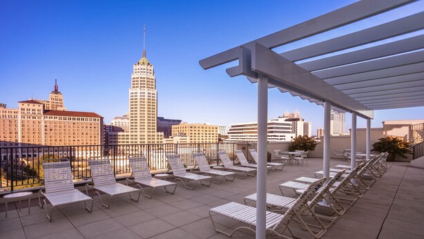 A rooftop terrace with sun loungers, a pergola, and a view of a city skyline including a prominent skyscraper.