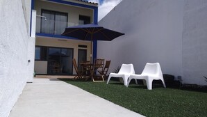 A patio with a table and chairs, a blue umbrella, and a small lawn area. - California House in Ribeira Grande (Ribeira Grande)
